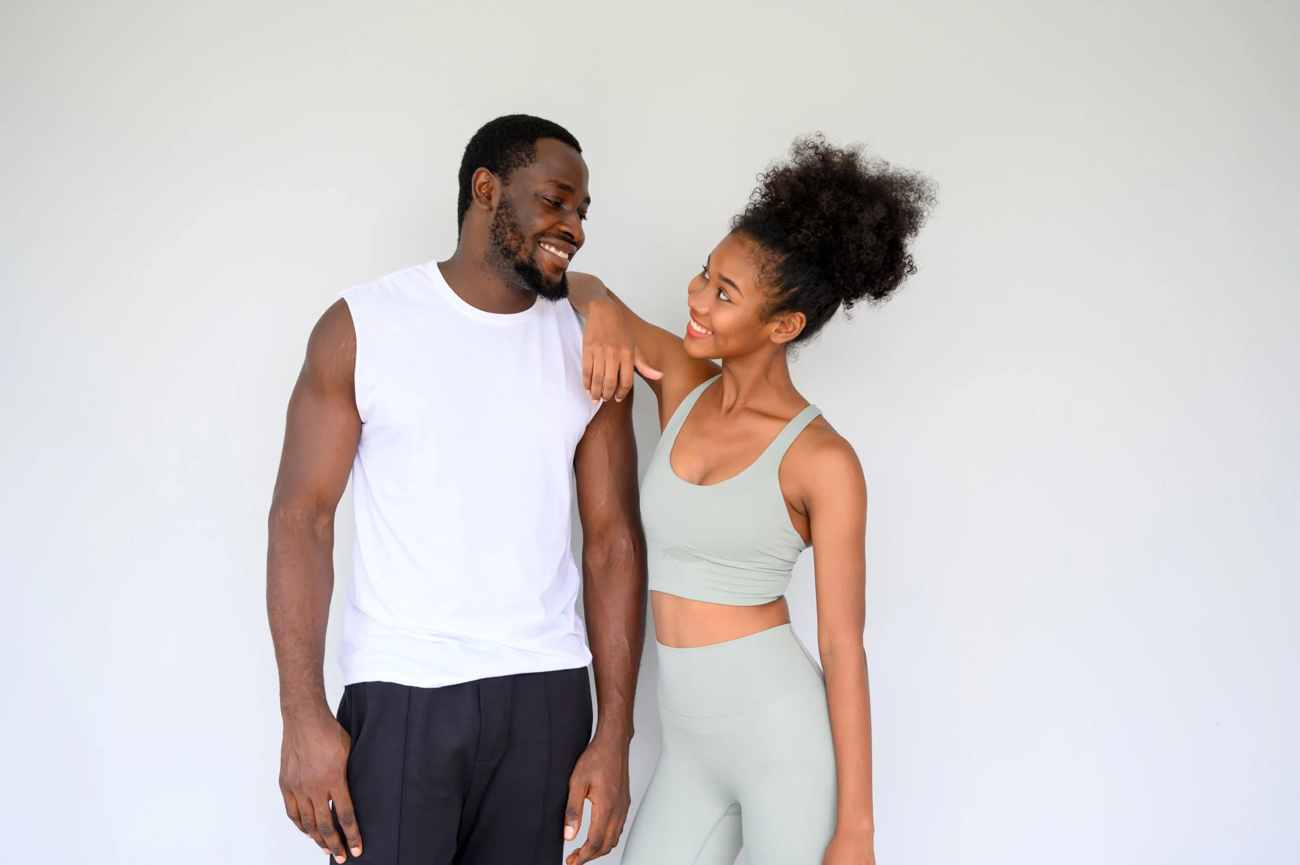Two smiling individuals share a joyful moment in athletic wear against a neutral background.